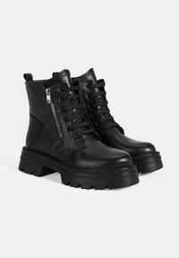 Bottines en cuir noir avec une finition texturée, bout rond, lacets sur le devant, fermeture éclair sur le côté et semelle épaisse et robuste.