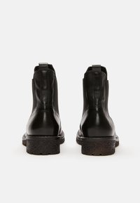 Botas de cuero negras hasta el tobillo con suela de goma texturizada, paneles laterales elásticos y tiradores; silueta elegante con acabado suave.
