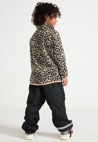 Fleecejakke i leopardmønster med lange ermer og høy krage, kombinert med svarte løse bukser med en reflekterende stripe på kanten.