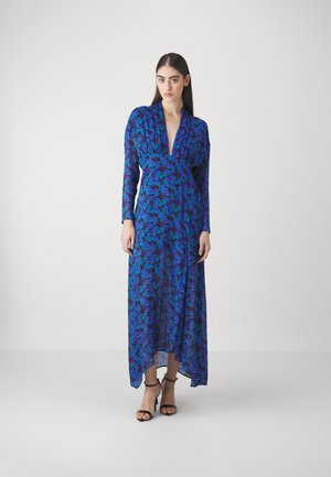 Long blue dress with floral pattern featuring purple and green details. V-neckline and long sleeves. Worn with black strappy sandals.
