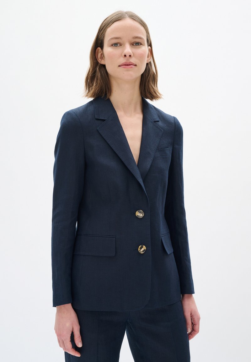 Námořnický lněný blazer s klopovým límcem, jednořadým zapínáním a zlatými knoflíky. Obsahuje dvě přední kapsy a přiléhavý střih.