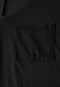 Débardeur en tricot noir avec une poche plate sur la poitrine gauche. Le tissu est lisse avec une texture subtile, et les bords sont finis avec un biais.