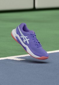 Μοβ αθλητικό παπούτσι με επάνω μέρος από δίχτυ, λευκές λεπτομέρειες και ροζ ελαστική σόλα, με σχέδιο κορδονιών και λογότυπο στο πλάι.