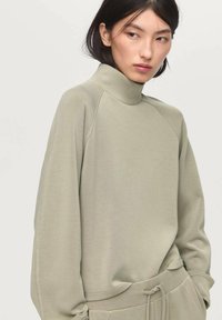 Sudadera de cuello alto en gris verdoso claro con mangas raglán. Tejido suave y liso con un corte relajado y detalles de costura mínimos.