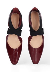 Bordeaux lakleren schoenen met een spitse neus en zwarte elastieken kruisbanden. Glad interieur met een contrasterende beige binnenzool.