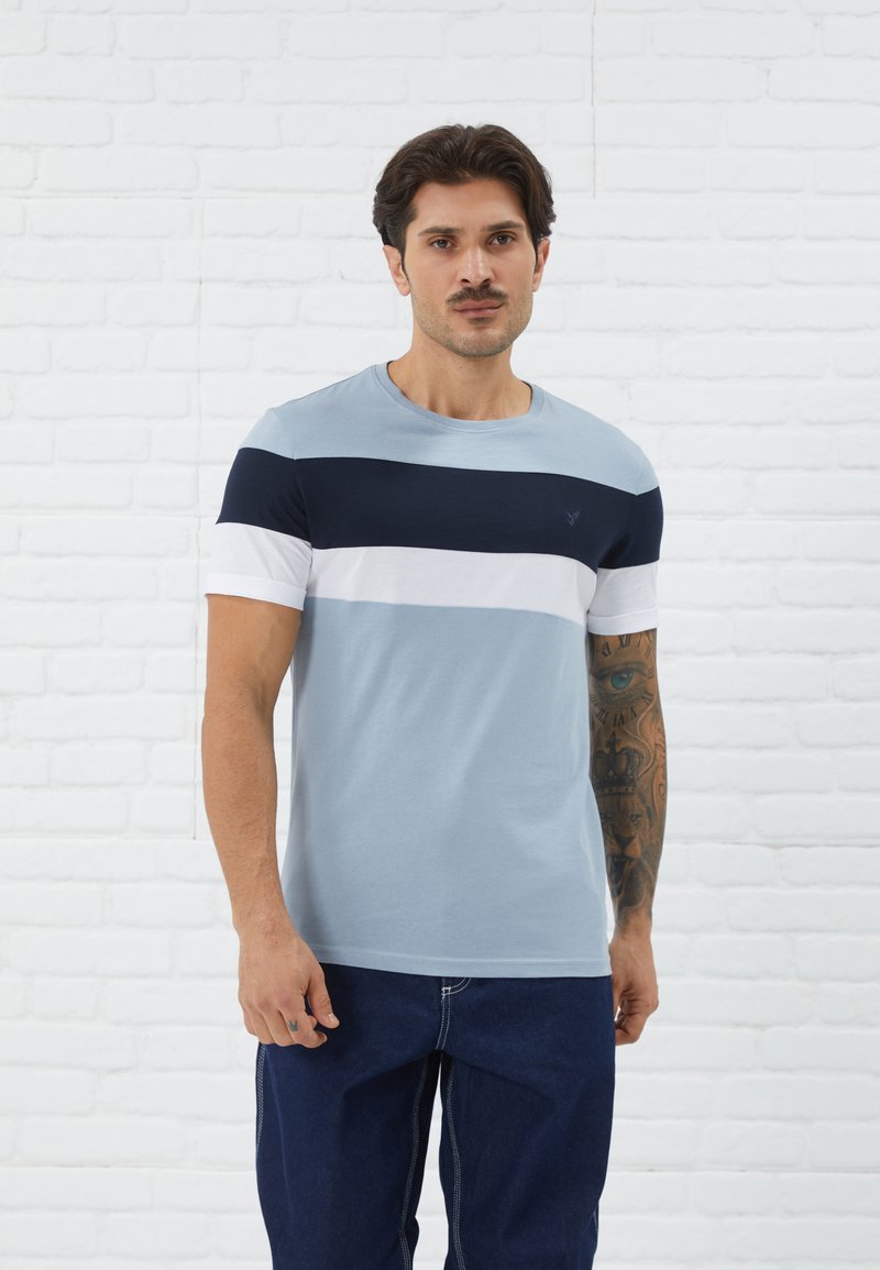 Camiseta de color azul claro con rayas horizontales en azul marino, blanco y azul claro, cuello redondo, mangas cortas y un logotipo decorativo en el pecho.