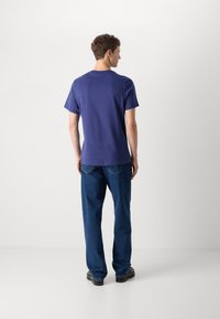 Purple cotton T-shirt with short sleeves, relaxed fit, and crew neckline, paired with blue denim jeans, shown from the back.