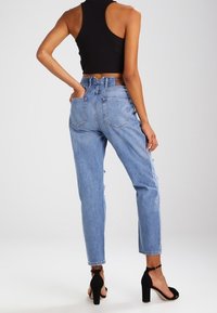 Vaqueros de mezclilla de cintura alta en azul claro con diseño de cinco bolsillos, desgastes en las piernas y corte recto. Combinados con sandalias de tacón negras.