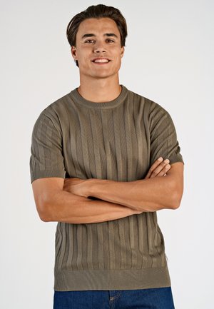 Khakifarbener, gerippter Kurzarm-Pullover mit Rundhalsausschnitt, strukturiertem Stoff und enganliegenden Bündchen, kombiniert mit blauen Denim-Jeans.