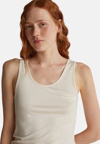 Beżowy bezrękawnik wykonany z miękkiego materiału, z okrągłym dekoltem i gładką fakturą, przylegający do ciała bez dodatkowych ozdób.