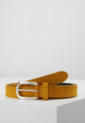 Ceinture en daim jaune moutarde avec boucle rectangulaire argentée, reposant enroulée sur une surface blanche sur un fond clair uni.