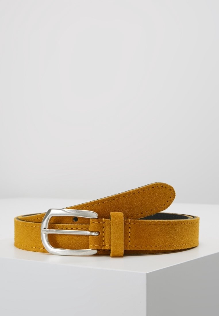 Ceinture en daim jaune moutarde avec boucle rectangulaire argentée, reposant enroulée sur une surface blanche sur un fond clair uni.