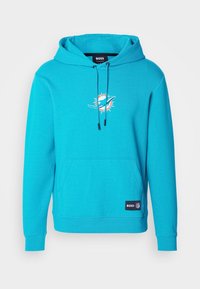 Tealfärgad hoodie med en framficka, justerbar dragsko och Miami Dolphins-logotyp på bröstet. Har ribbade muddar och nederkant.