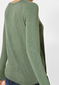 Long-sleeve top in a muted green fabric; features a round neckline with a subtle textured detail along the collar and sides.