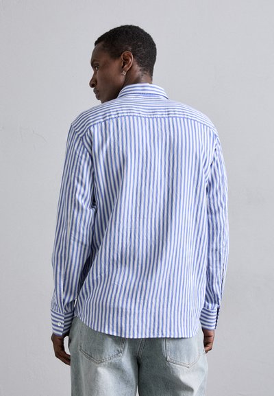 Camisa a rayas en algodón azul y blanco, de manga larga, con cuello abotonado, corte relajado, con un dobladillo redondeado y detalle en el yugo trasero.