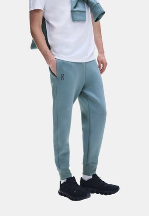 Personne portant un pantalon de jogging bleu clair, des chaussettes blanches, des baskets noires et un t-shirt blanc avec un sweat bleu clair assorti drapé sur les épaules.
