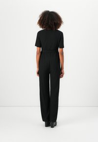 Svart jumpsuit med korte ermer, tettsittende midje og vide ben. Teksturert stoff, ingen synlige mønstre eller detaljer. Minimalistisk design.