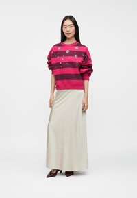 Sweatshirt riscado em rosa e bordô com embellishments, combinado com uma saia maxi bege clara e sapatos de salto bordô. Texturas suaves por toda a parte.