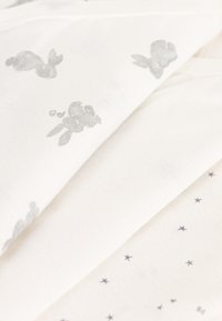 Tejido blanco con impresiones de conejitos grises y pequeñas estrellas oscuras, con una textura suave y un acabado liso. Dos capas superpuestas parcialmente.