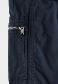 Marinblå jacka i tyg med en texturerad ytfinish, med en sidoficka med en silverfärgad dragkedja och förstärkningsstygn.
