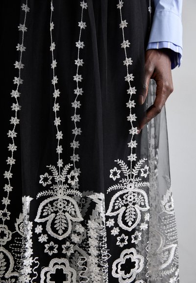 Svart, gjennomsiktig skjørt med intrikate, hvite blomsterbroderier, og et mønster av stjerneaktige motiver over stoffet, samt en lagdelt tekstur.