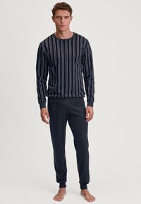 Marineblauwe lange mouw top met verticale strepen in rood en wit, gecombineerd met effen marineblauwe broek, beide gemaakt van gladde stof.