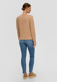 Beige langärmeliger Pullover mit Rundhalsausschnitt, kombiniert mit blauen Skinny Jeans und hellbraunen Plateausneakern, von hinten betrachtet.