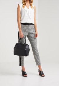 Czarna skórzana torebka o strukturalnym kształcie, gładkiej fakturze i podwójnych uchwytach. Nosi ją osoba w białej bezrękawnikowej bluzce i spodniach w kratkę.