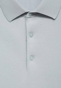 Tricou polo gri deschis cu un guler texturat, trei butoane și un material moale. Designul este simplu, având accente ribbate pe guler.