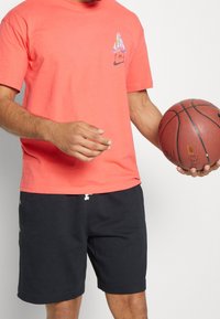 Coral cotton t-shirt with a small multicolored sail graphic and Nike logo, paired with navy shorts featuring a drawstring and side buttons.