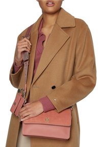 Růžová kabelka s texturovaným materiálem a hladkým klopou, spárovaná s odpovídajícím držákem na karty. Obsahuje stříbrné logo a nastavitelné ramenní popruhy.