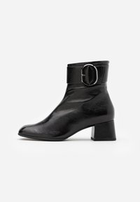 Botines de cuero negro con punta redondeada, una ancha correa con hebilla en el tobillo y un tacón grueso, con una superficie texturizada.