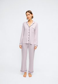 Set de pijamale lila deschis, cu bluză cu dungi lungi, cu nasturi, având accente negre și buzunar, asociat cu pantaloni largi asortati și manșete largi.