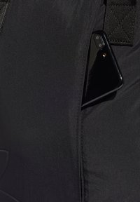 Crna tkanina torba s glatkom teksturom, koja sadrži vidljiv crni pametni telefon djelomično umetnut u bočnu džep.
