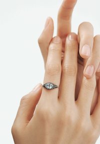 Anillo de aguamarina con corte ovalado, montado en una banda de plata texturizada con un intrincado diseño y pequeños acentos negros, llevado en una mano.