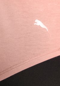 Light pink athletic fabric with a smooth texture, featuring a white Puma logo; black accents at the bottom; flatlock seams visible.