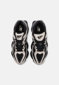 Black and beige athletic shoes with mesh and synthetic overlays. Features a cushioned sole and black laces. Model number visible on the tongue.