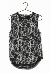 Top senza maniche in pizzo bianco e nero, caratterizzato da motivi floreali, scollo rotondo e orlo leggermente curvo. Appeso a un gancio nero.