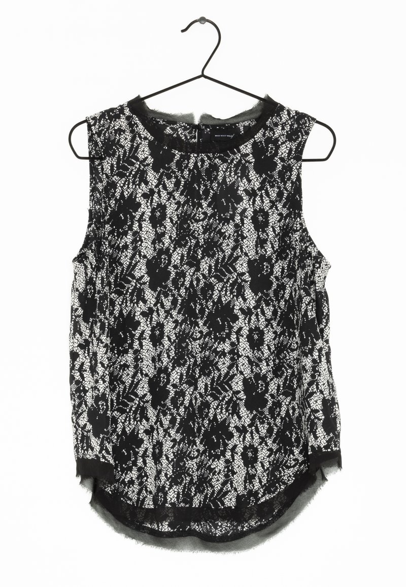 Top senza maniche in pizzo bianco e nero, caratterizzato da motivi floreali, scollo rotondo e orlo leggermente curvo. Appeso a un gancio nero.