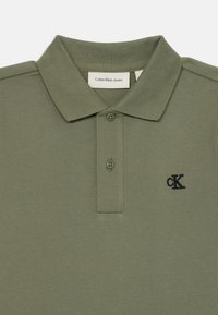 Olivgrünes Poloshirt aus strukturiertem Stoff, mit klassischem Kragen, drei Knöpfen und einem kleinen, auf der Brust gestickten schwarzen Logo.