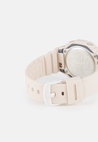 Beige silicone watch with a silver stainless steel back. Features a textured strap with holes and a white buckle for closure.