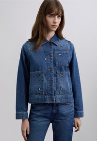 Denimjakke i blå vask, dekoreret med farverige perler foran, fire lommer, knaplukning foran og krave.