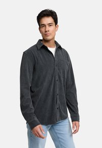 Camisa de pana gris oscuro con botones al frente, cuello puntiagudo, un bolsillo en el pecho y textura acanalada; combinada con jeans de color azul claro.