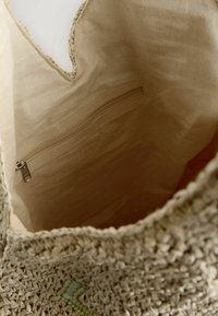 Vävd beigefärgad tote bag med öppen topp, som har ett litet innerfack med dragkedja och ett strukturerat stygnmönster längs den övre kanten.