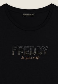 Camiseta de algodón negra con la palabra "FREDDY" en strass y "sé tú mismo" en una fuente manuscrita, cuello redondo y textura suave.