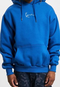 Sudadera azul con capucha hecha de una mezcla de algodón. Cuenta con un bolsillo frontal, puños y dobladillo acanalados, y un logo blanco bordado en el pecho.