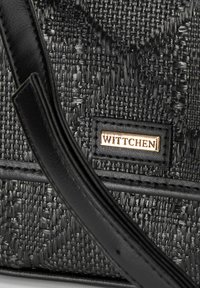 Borsa a mano nera intrecciata con un motivo testurizzato, dotata di una placca con logo in tonalità oro e una tracolla in pelle nera. Design compatto e strutturato.