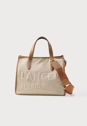 Beżowa torba na ramię z płótna z brązowymi skórzanymi uchwytami i paskiem, z tłoczonym napisem "LANCEL PARIS 1876" na przodzie.