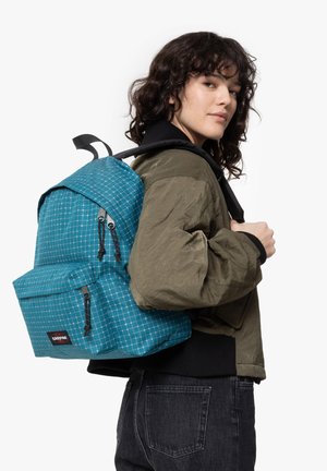 Teal patterned backpack with a grid design, featuring two zippered pockets, adjustable straps, and a top handle, worn over an olive jacket.