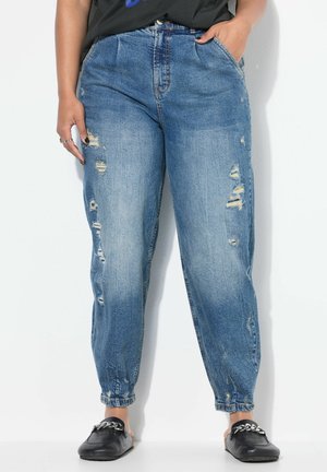 Pantaloni jogger in denim azzurro chiaro con strappi e caviglia affusolata. Presentano una vita alta, tasche e un orlo risvoltato. Scarpe nere slip-on.